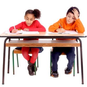 two young students sitting side by side at a desk and writing
