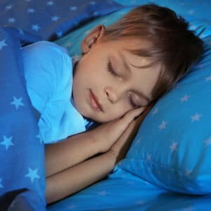 Child sleeping on his side in bed his hands folded under his head