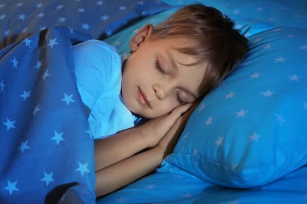 Child sleeping on his side in bed his hands folded under his head