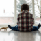 Small child in a flannel shirt and jeans sitting on the floor with his back to the camera and his legs spread apart