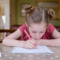 Young girl with pencil in hand bending over while practicing her handwriting