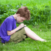 Young boy sitting in the grass writing on a note with a pen