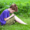 Young boy sitting in the grass writing on a note with a pen