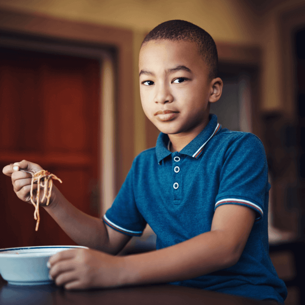 Young child looking into the camera as he raises a spoonful of spaghetti to eat
