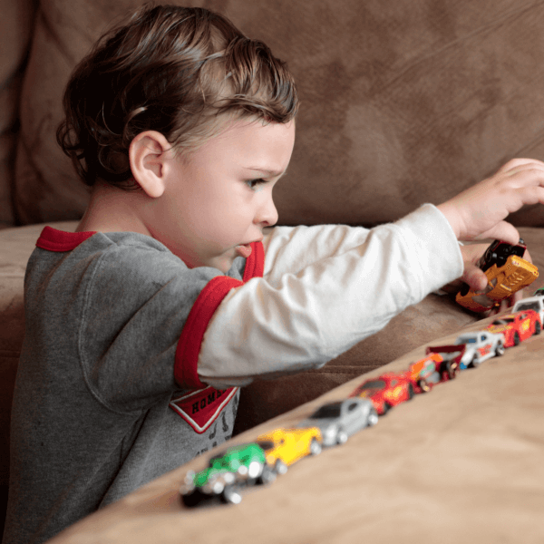 Small child playing with a row of toy cars