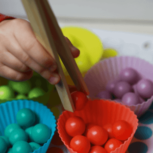 Child moving colored balls between different bowls
