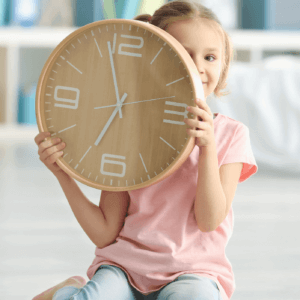 Small child sitting on the floor and holding a large analog clock